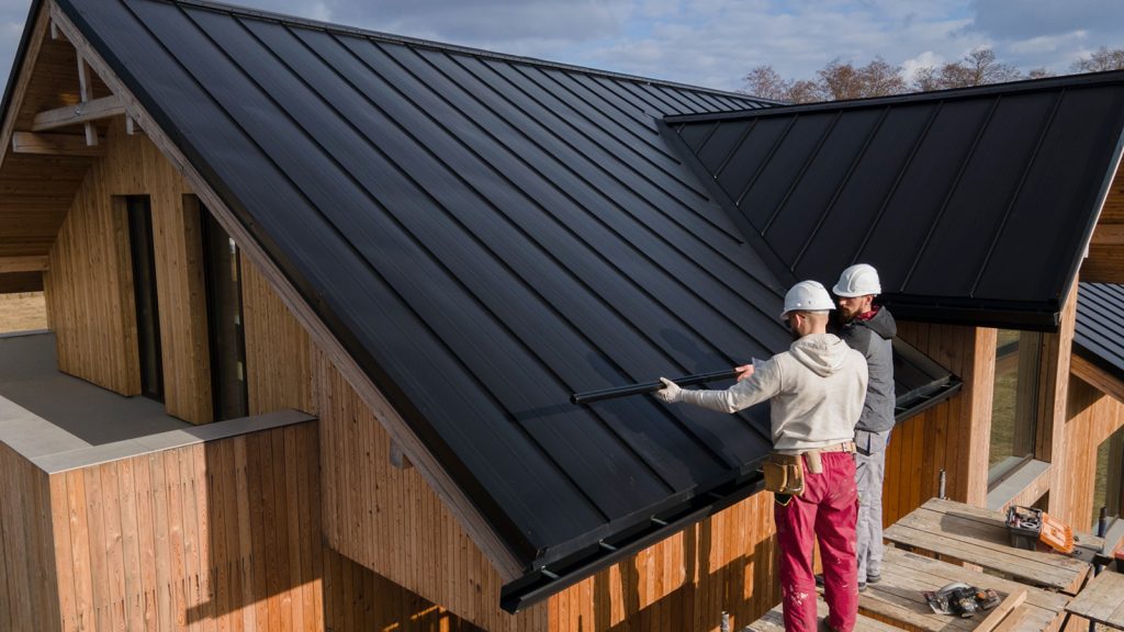 Workers installing a black metal roof on a wooden conservatory, emphasizing roofing upgrades for improved energy efficiency and comfort.
