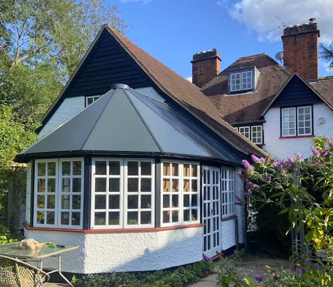 Insulated conservatory with a modern roof design, featuring large windows and a stylish exterior, surrounded by greenery and flowers, enhancing year-round comfort and energy efficiency.