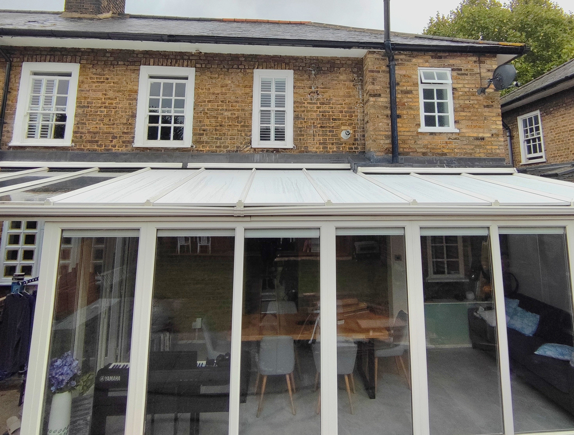 Insulated conservatory with white roof panels and glass walls, showcasing a modern dining area and natural light, enhancing energy efficiency and comfort for year-round use.