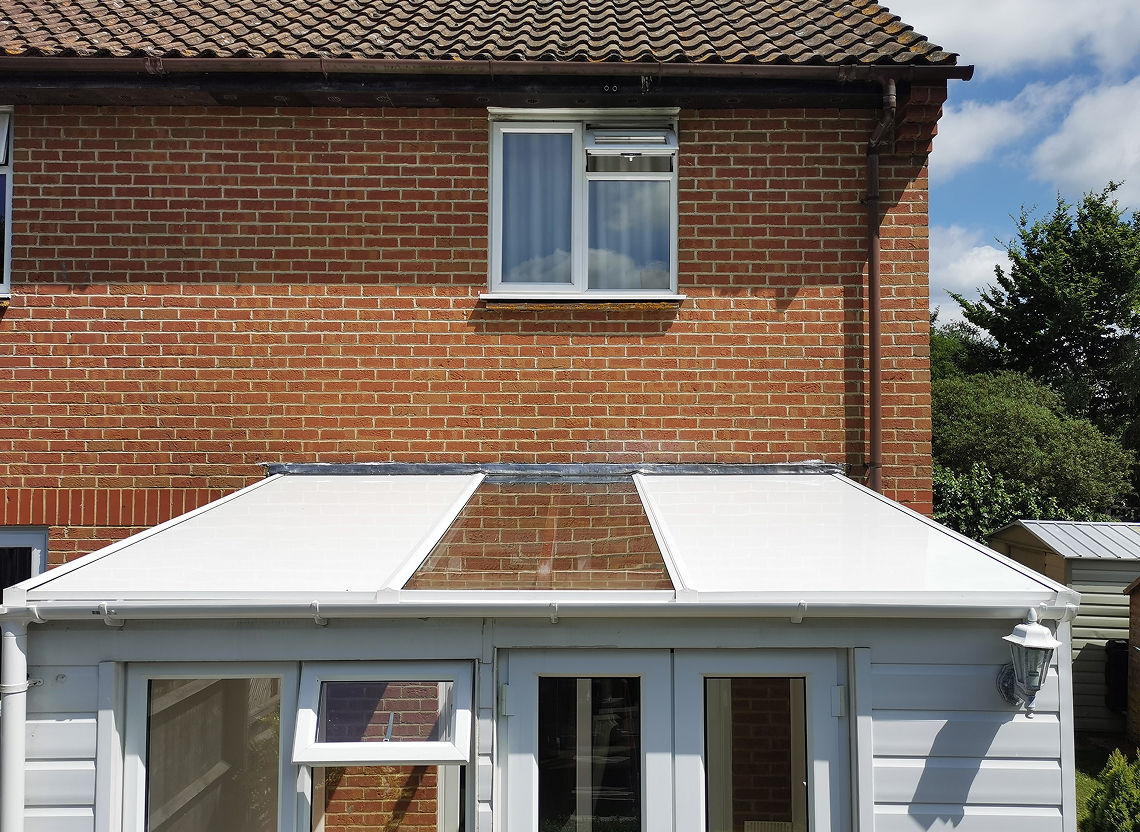 Insulated lean-to roof panels installed on a conservatory, showcasing a white roof structure against a brick wall, emphasizing energy efficiency and comfort.