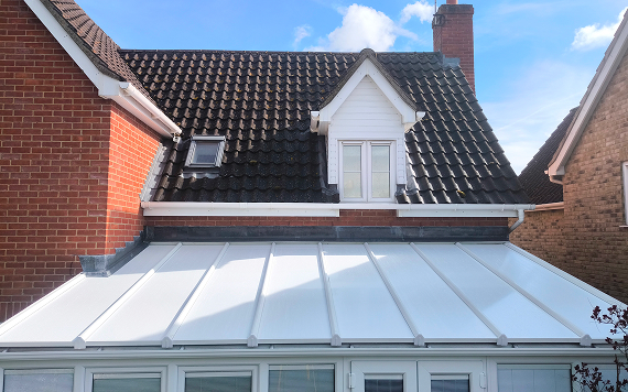 Insulated lean-to conservatory roof panels installed on a home, showcasing a modern design with a white finish, complementing the surrounding brick and tiled structure.