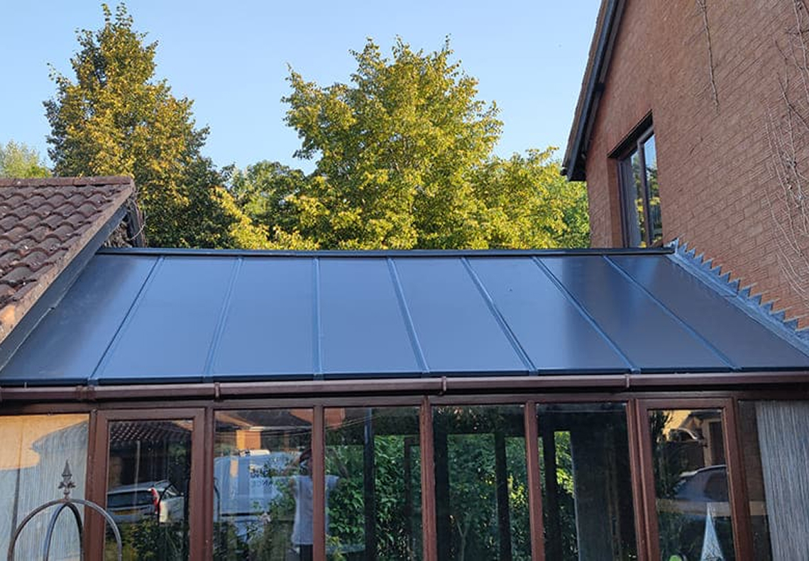 Insulated conservatory roof panels by Rosy Roof, showcasing energy-efficient design and enhanced property aesthetics against a backdrop of trees and clear sky.
