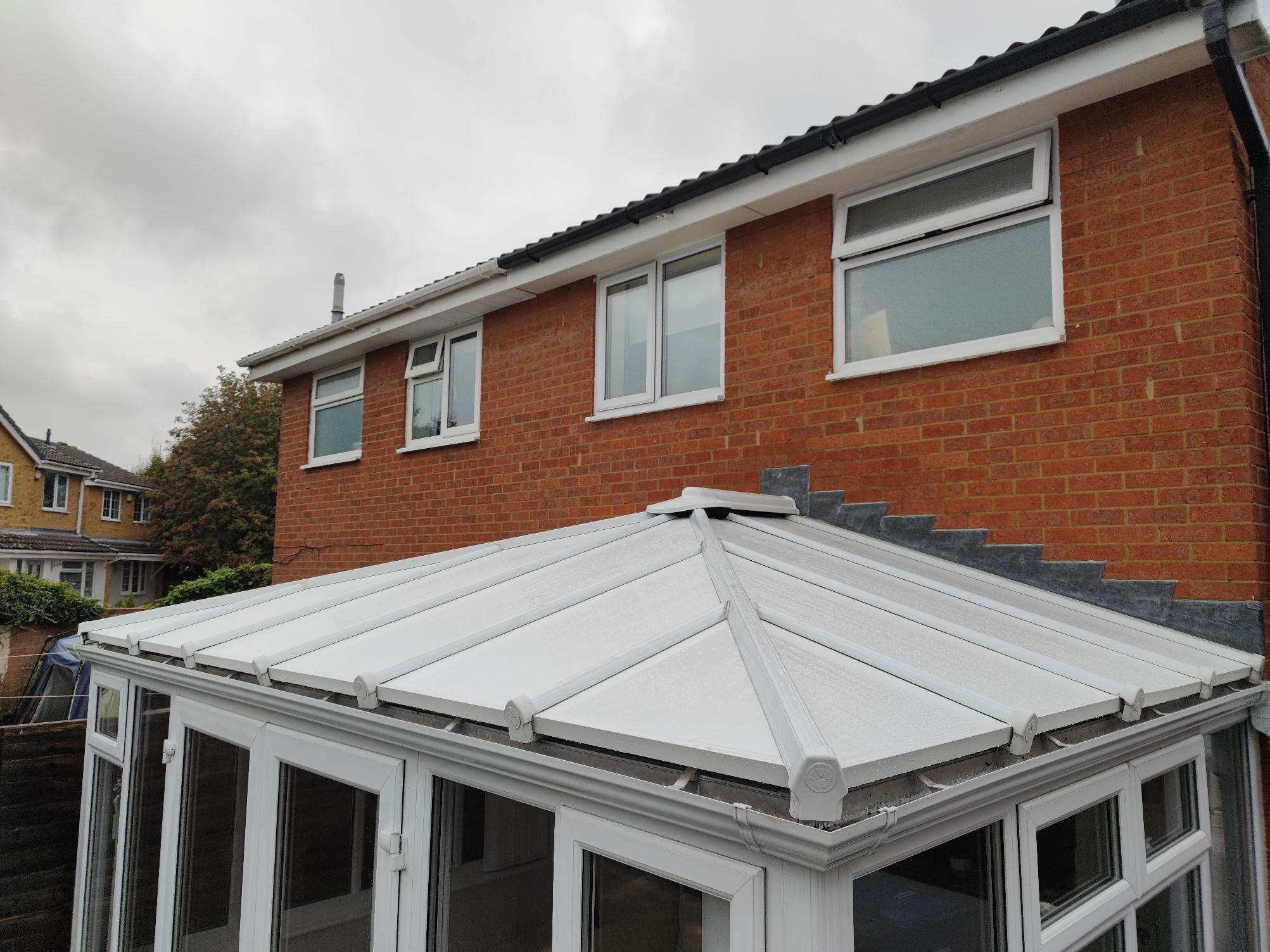 Insulated conservatory roof transformation showcasing a modern white roof structure attached to a red brick home, emphasizing energy efficiency and aesthetic appeal.