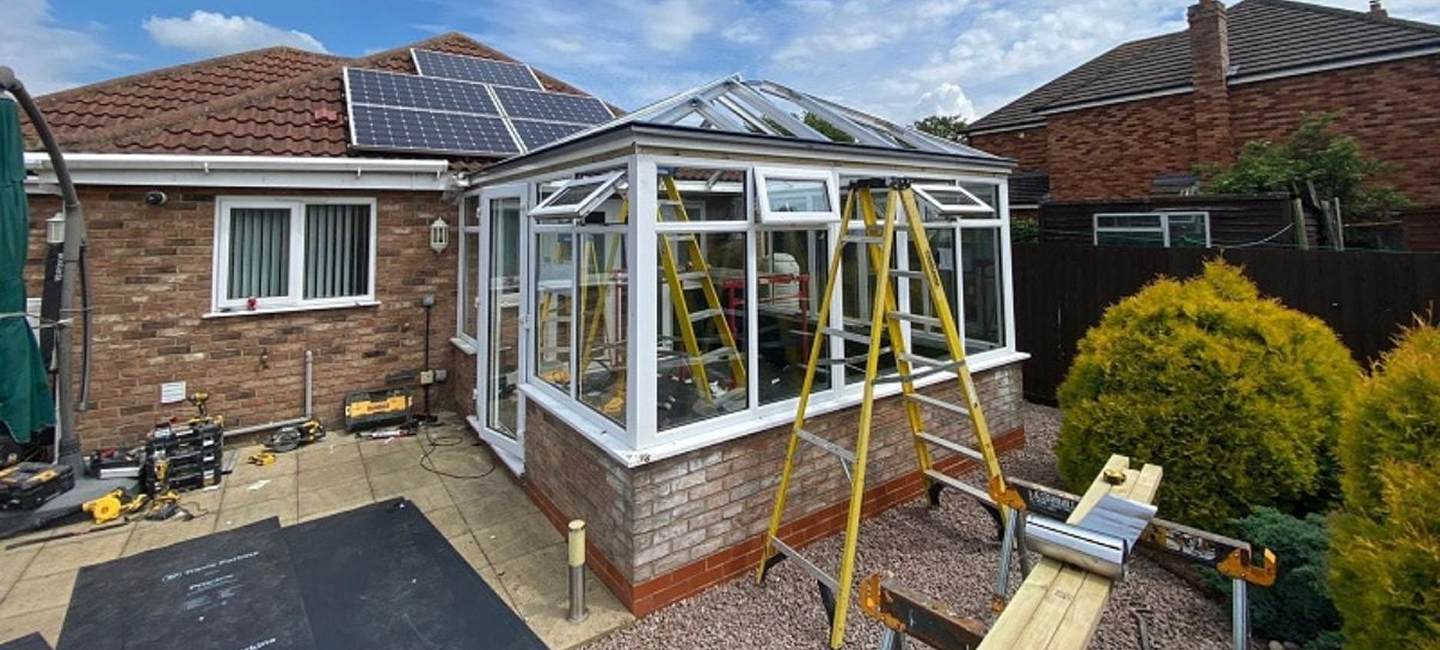 Conservatory roof replacement project in progress, featuring a partially constructed glass roof, ladders, and tools, highlighting home improvement efforts for enhanced energy efficiency and comfort.