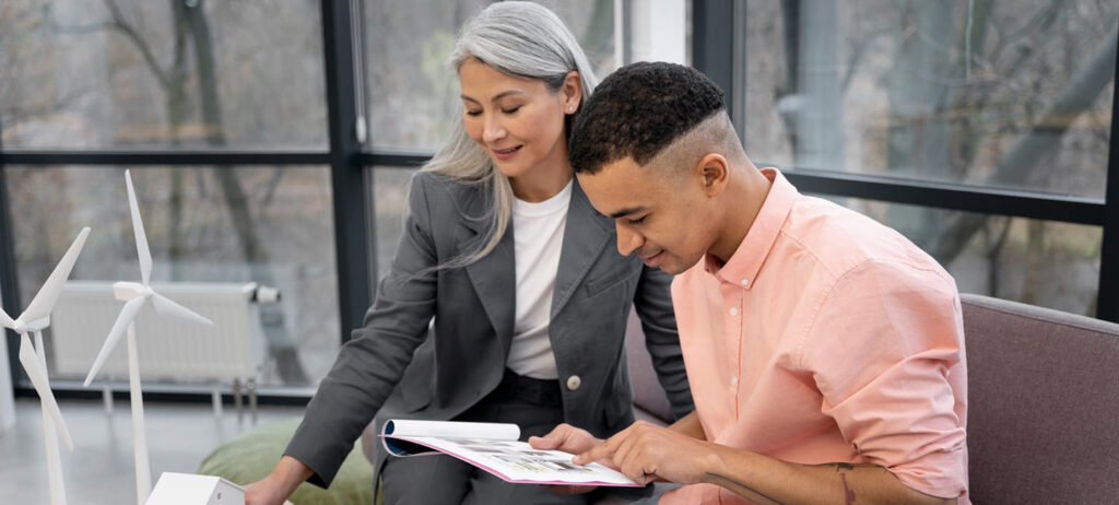 Two individuals discussing conservatory roof upgrades, examining a brochure, with a model wind turbine in the foreground, highlighting energy efficiency and home improvement.