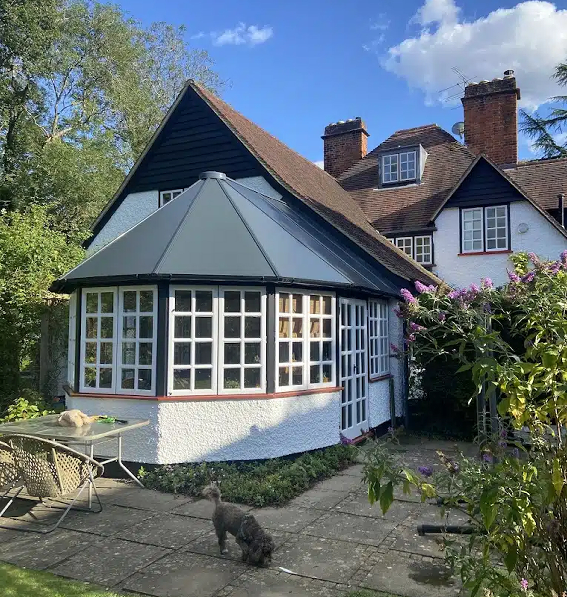 Conservatory with a modern grey roof, surrounded by greenery and a dog in the garden, showcasing a stylish and energy-efficient design for Rosy Roof's services in Northampton.